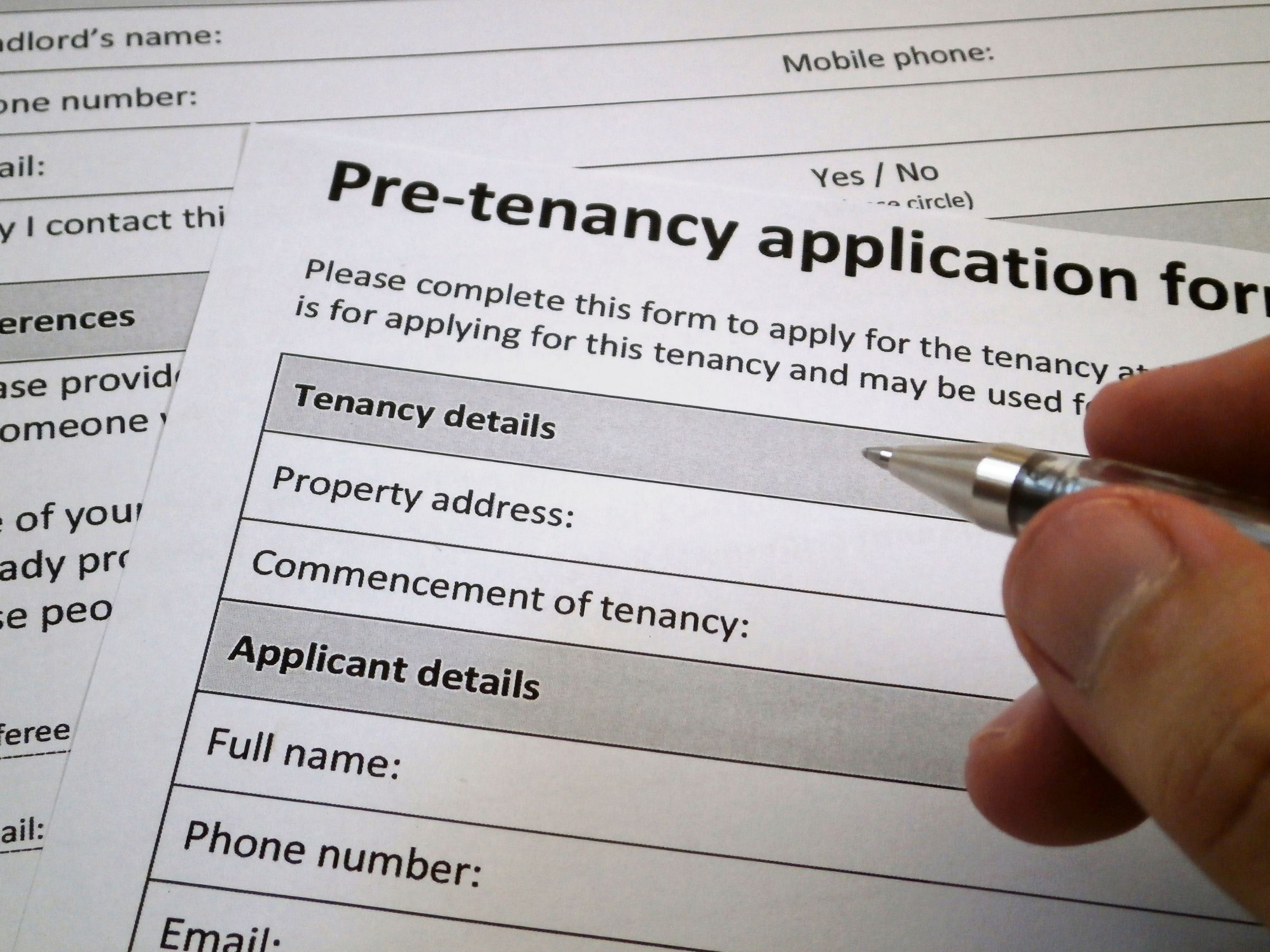 Person filling out a pre-tenancy application form with a pen, focusing on the section for tenancy details and applicant information.