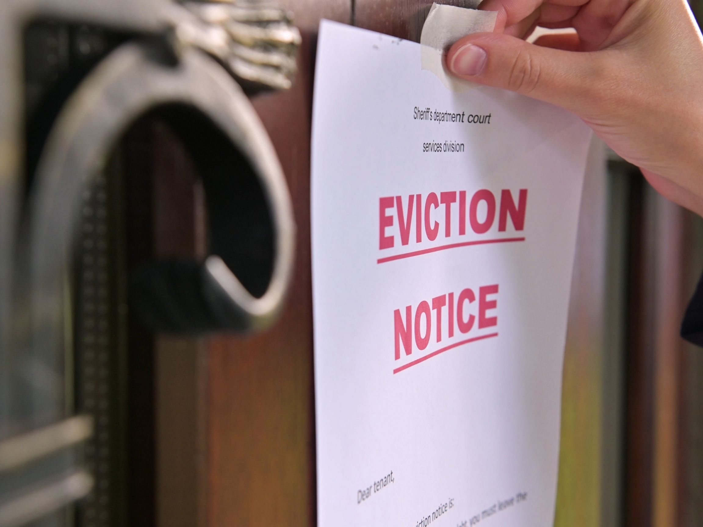 Close-up of a hand posting an eviction notice on a door, with the word 'Eviction Notice' prominently displayed in bold red letters.