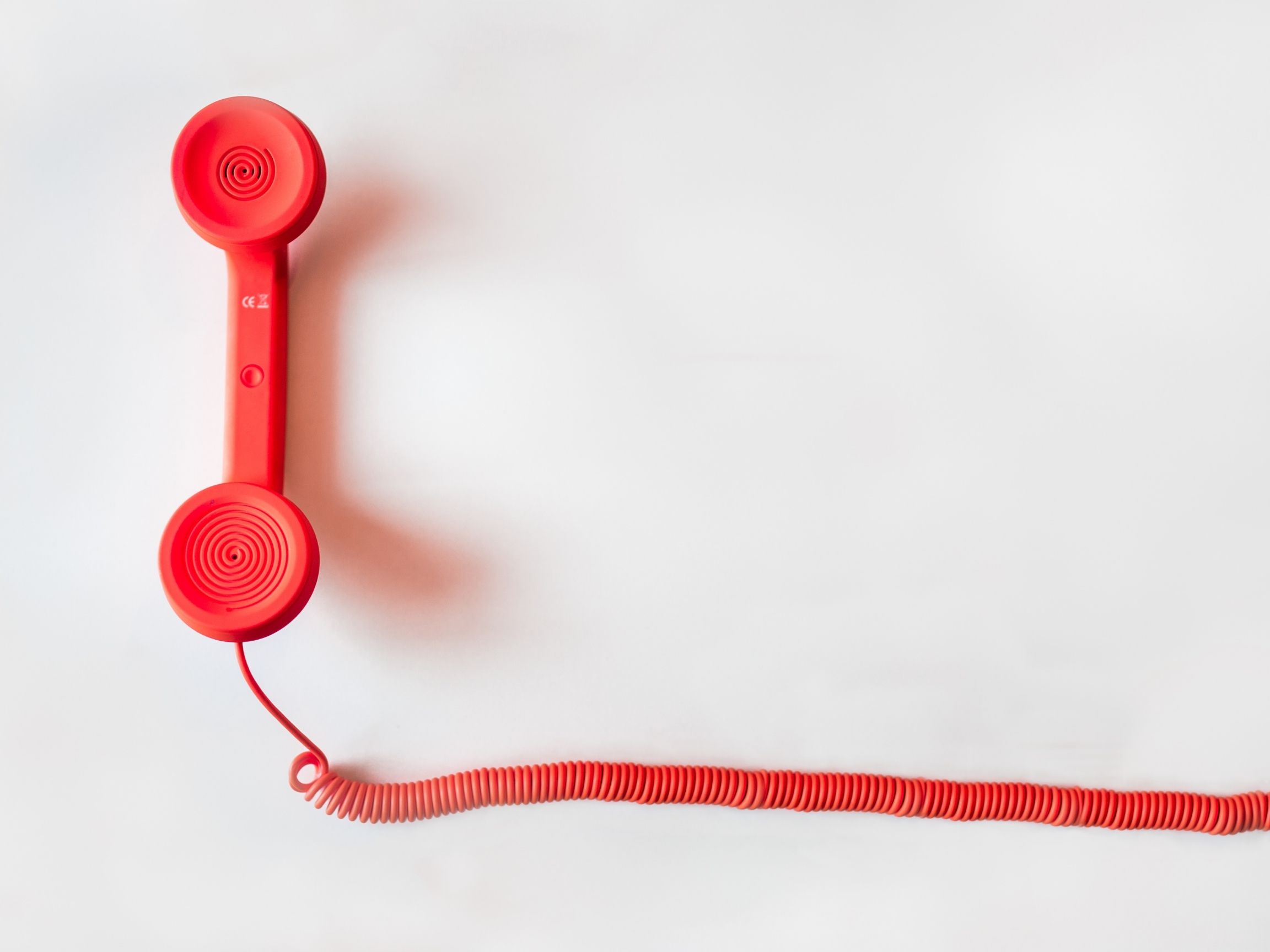 Bright red telephone handset with a coiled cord against a white background.